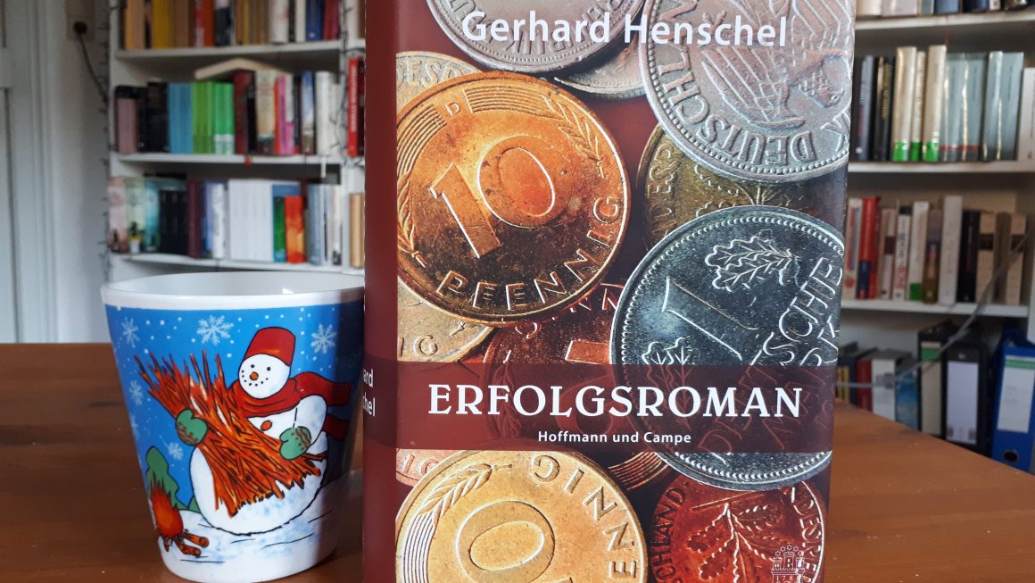 Das Bild zeigt den Roman "Erfolgsroman" von Gerhard Henschel. Links daneben steht die Schneemanntasse.