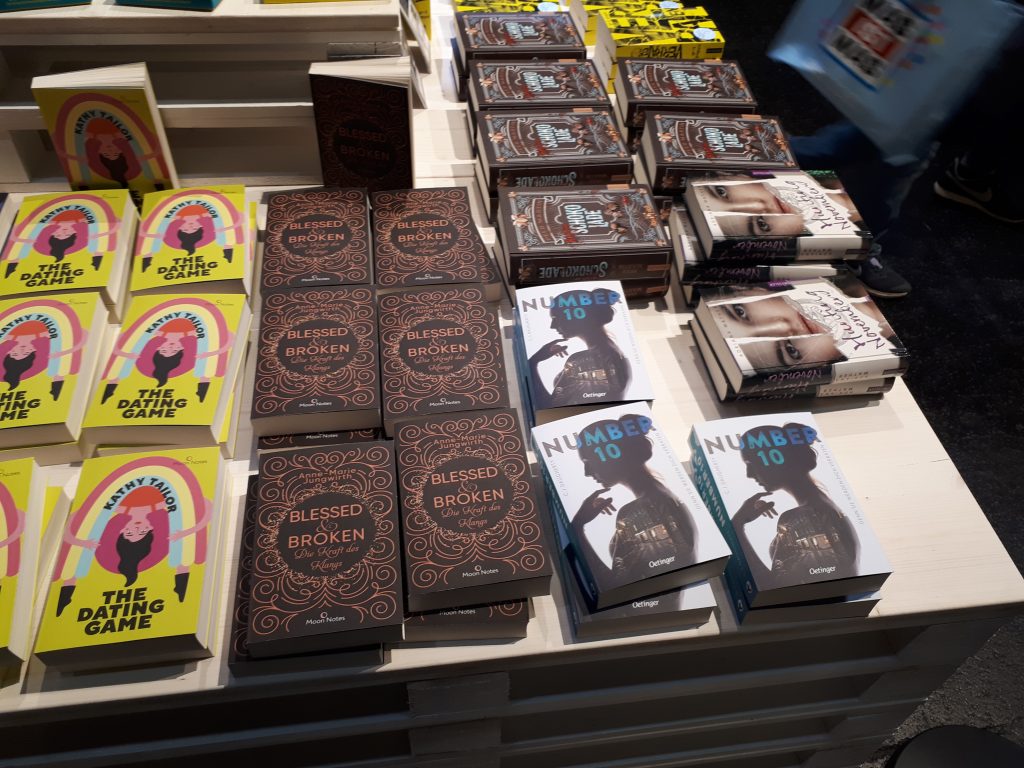 Das Bild zeigt Bücher des Oetinger Verlags. Von Links nach Rechts sind dies: "The Dating Games" von Kathy Tailor, "Blessed & Broken. Die Kraft des Klangs" von Anne-Marie Jungwirth und "Number 10" von C.J. Daugherty.