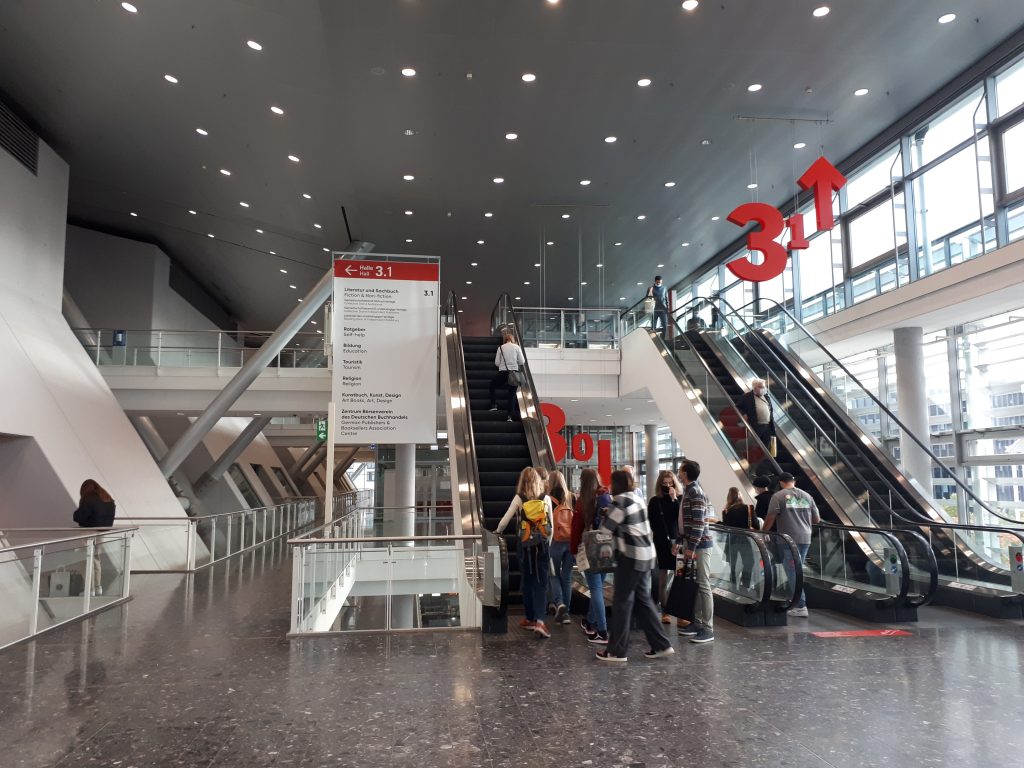 Das Bild zeigt den Treppenauf und abgang zu den Hallen 3.1 und 3.0 auf dem Messegelände Frankfurt am Main. Auf den Rolltreppen sind ein paar Menschen