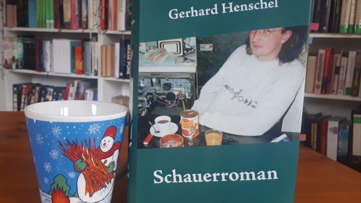 Das Bild zeigt das Buch "Schauerroman" von Gerhard Henschel. Das Cover ist in einem Dutch Angle und zeigt eine alte Aufnahme des Autors. Daneben steht die Schneemanntasse.