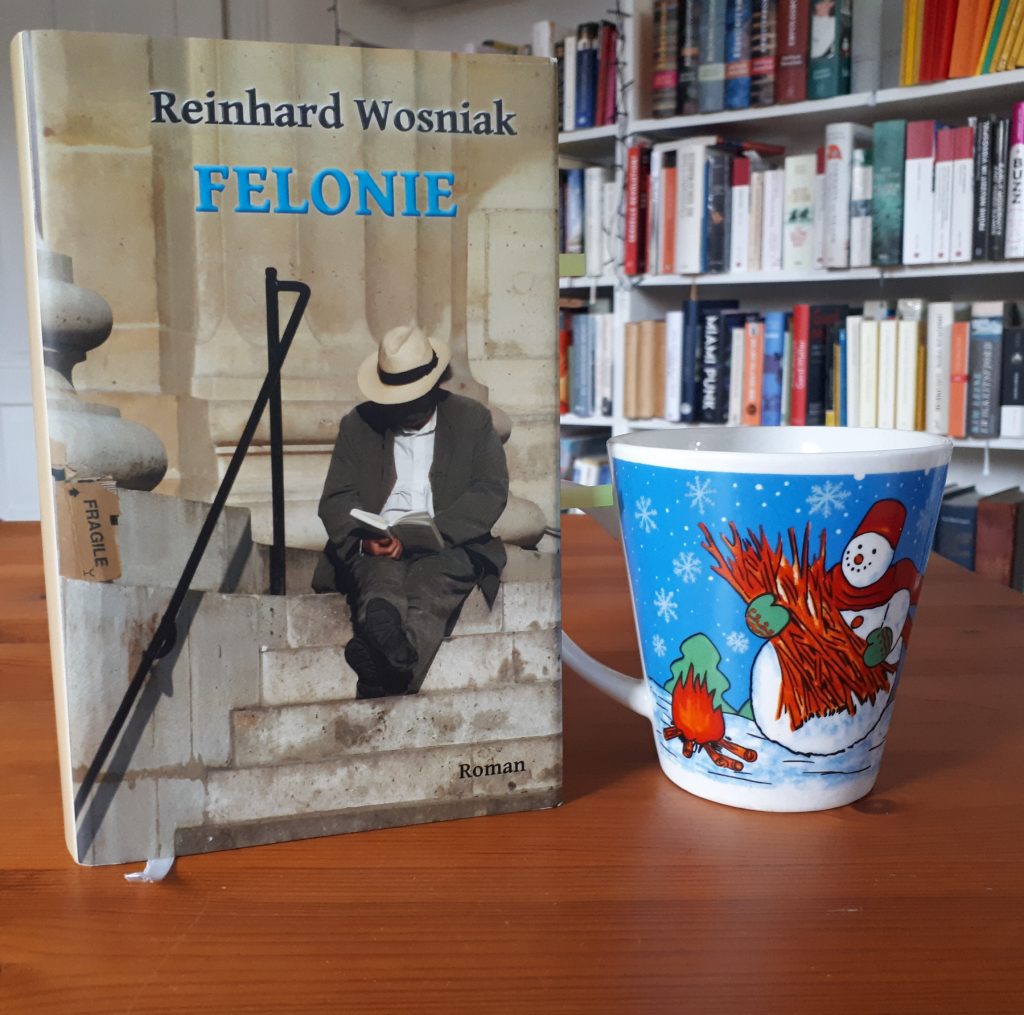 Das Bild zeigt das Buch "Felonie" von Reinhard Wosniak. Daneben steht die Schneemanntasse. 