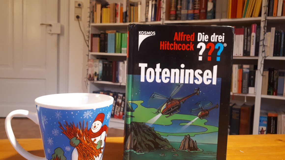 Das Bild zeigt das Buch "Toteninsel" von Andrè Marx. Links daneben steht die Schneemanntasse