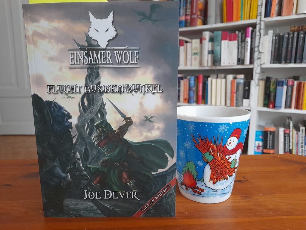 Das Bild zeigt das Buch "Einsamer Wolf: Flucht aus dem Dunkel" von Joe Dever. Daneben steht die Schneemanntasse. 