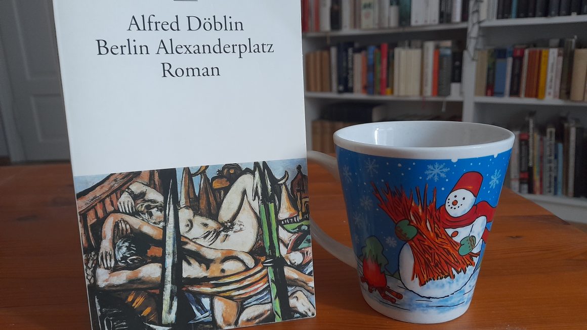 Das Bild zeigt eine Ausgabe von "Berlin Alexanderploatz" von Alfred Döblin. Daneben steht die Schneemanntasse.
