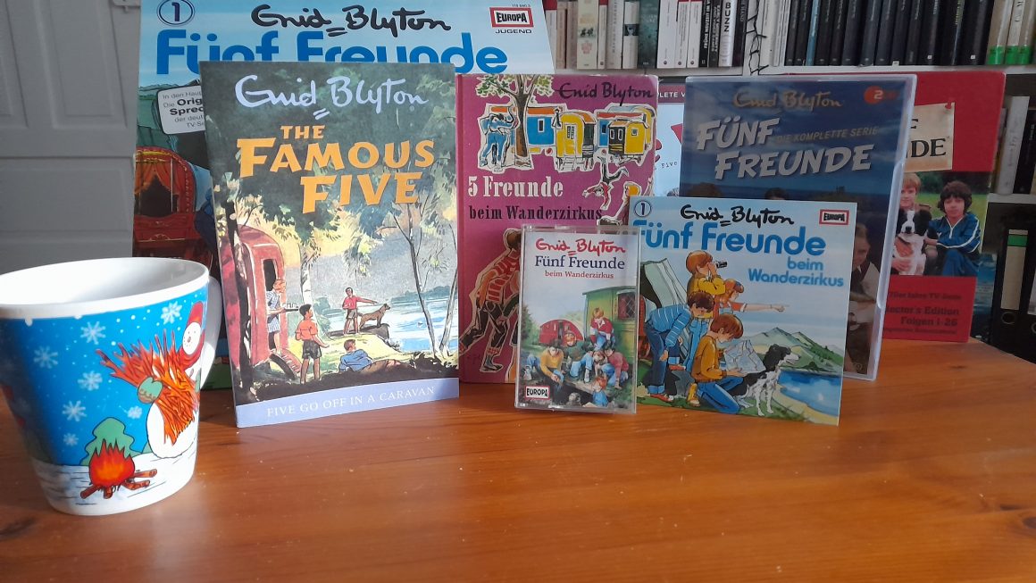 Auf dem Bild sind unterschiedliche Medien. Das Bild zeigt das Buch Five go off in a caravan" Dazu dann die deutsche Übersetzung "5 Freunde beim Wanderzirkus". Es sind die Hörspielfassungen von "5 Freunde bei Wanderzirkus" abgeboildet in Form der Schallplatte, der CD mit dem COver der Schallplatte und einer Kassette aus den frühen 1990ern. Im Hintergrund sind die DVD Boxen für die TV Serien aus den 1970ern und 1990er Jahren