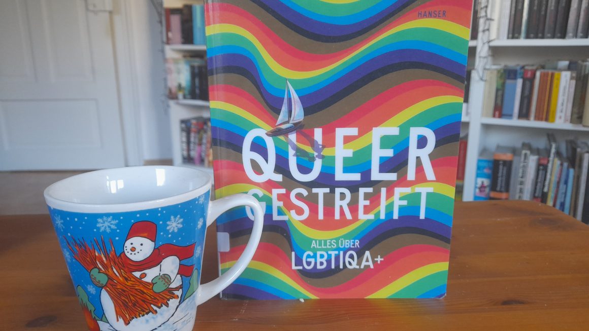 Das Buch "Queergestreift - Alles über LGBTIQA+" von Kathrin Köller und Irmela Schautz. Daneben steht die Schneemanntasse.